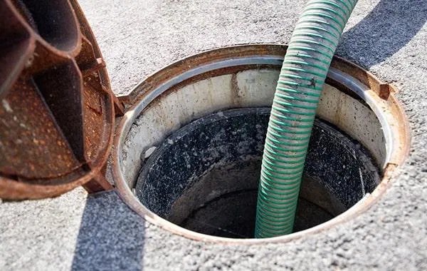 Manhole grease interceptor being serviced with a green suction hose in Dallas