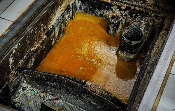 Open grease trap filled with orange grease and pipes at a Dallas restaurant